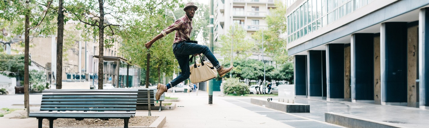 молодий чорношкірий чоловік стрибає з сумкою