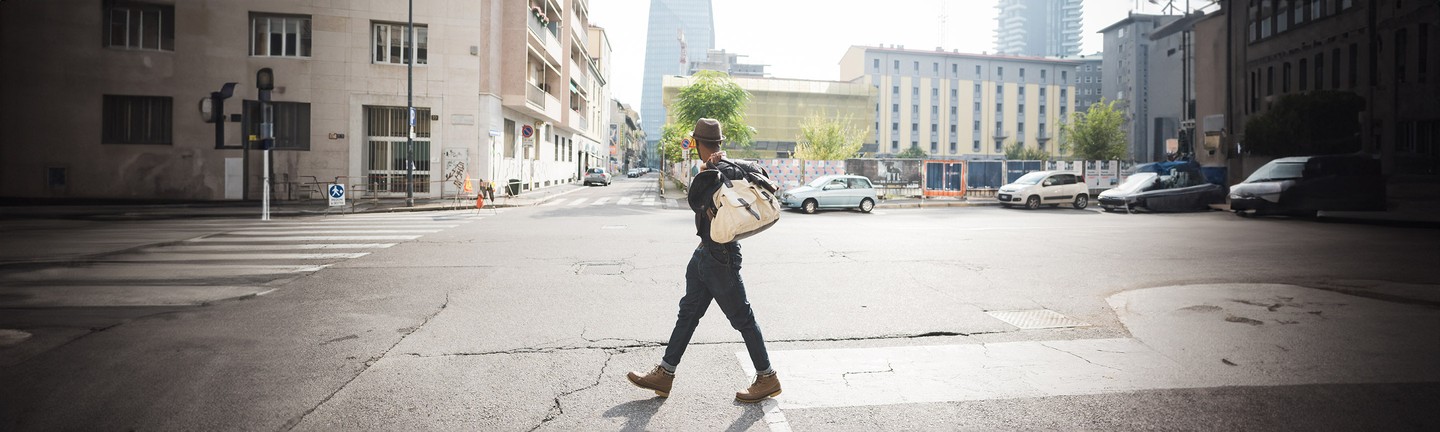 Молодой чернокожий мужчина идет с сумкой по улице