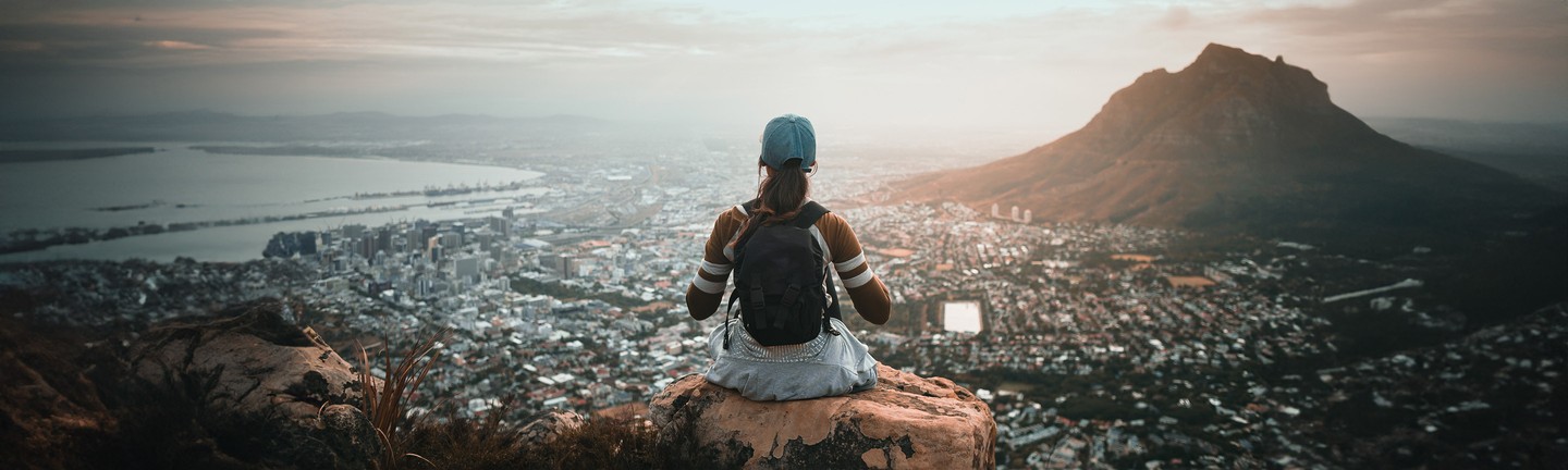 Young woman sitting with backpack overlooking city view at sunrise